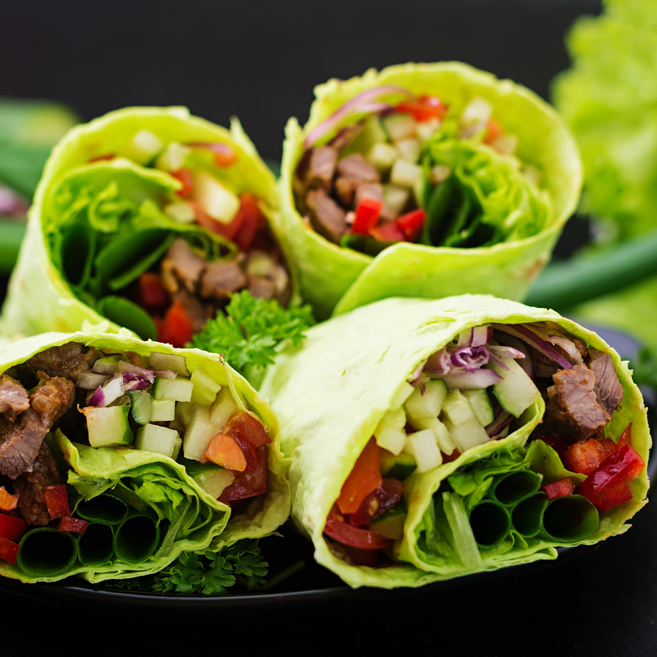 Four vibrant green wraps filled with beef, lettuce, diced cucumbers, red peppers, and red onions.